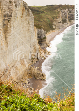 Steep limestone cliffs and coastal shoreline of Etretat in Normandy, France, overlooking waves and rugged beach. Steep limestone cliffs and coastal shoreline of Etretat in Normandy, France, overlooking waves and rugged beach. 133204607