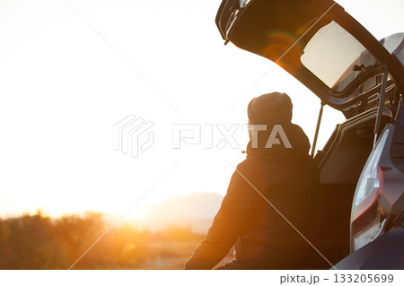 車のトランクを開け朝日を眺める男性 133205699