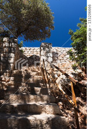 A rugged stone staircase climbs beside a weathered stone wall under a clear blue sky A rugged stone staircase climbs beside a weathered stone wall under a clear blue sky 133206666