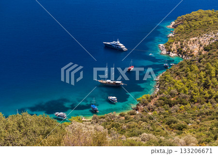 Aerial shot of a tranquil bay where several boats and yachts rest near a rocky coast 133206671