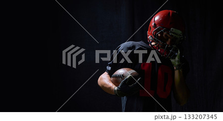 Football player holding ball with emotional fatigue in dramatic low light 133207345