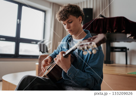 Teenage boy playing acoustic guitar in school music room. 133209026