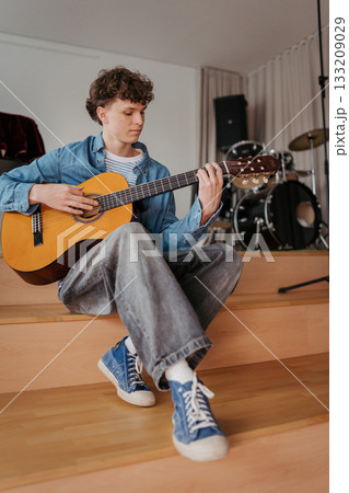 Teenage boy playing acoustic guitar in school music room. 133209029