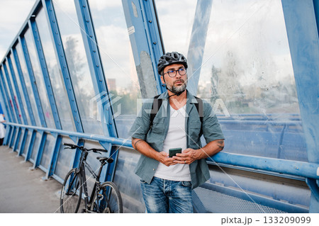 Bearded cyclist using phone while waiting for bus. 133209099