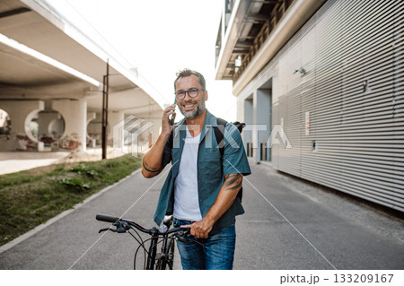 Male cyclist making phone call, standing by his bike. 133209167