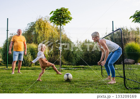 Little boy playing football with mother and grandfather in backyard. Little boy playing football with mother and grandfather in backyard. 133209169