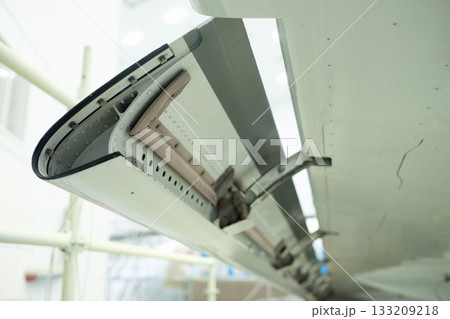 Aircraft wing flap mechanism detailed view showing aircraft maintenance environment with tools and equipment in the background during daytime Aircraft wing flap mechanism detailed view showing aircraft maintenance environment with tools and equipment in the background during daytime 133209218