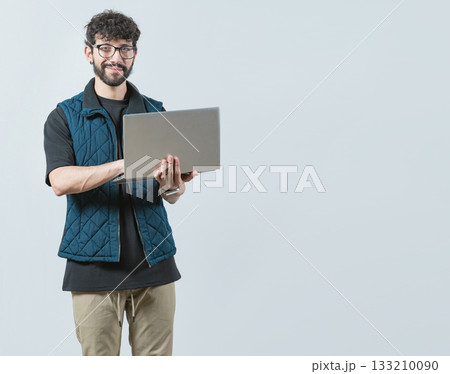 Smiling Bearded guy using laptop and looking at camera isolated. Handsome young man with glasses laptop and looking at camera 133210090