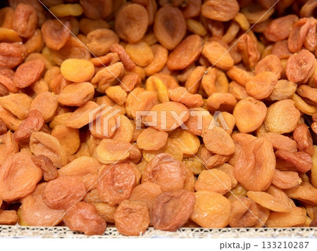 Lots of delicious plump golden orange dried apricots piled up on a tray for sale in a supermarket. Close-up. Lots of delicious plump golden orange dried apricots piled up on a tray for sale in a supermarket. Close-up. 133210287