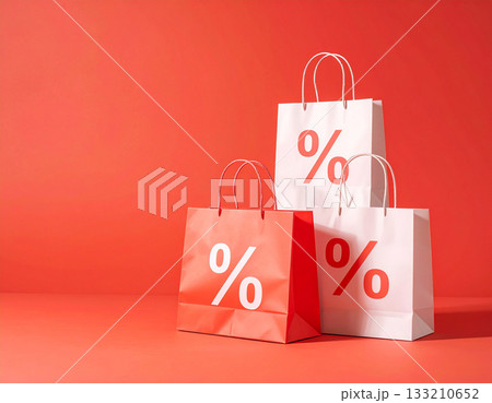 A stack of shopping bags with percentage discount symbols sits on a plain red background, representing big savings. 133210652
