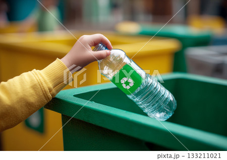 A child's small hand placing a plastic bottle into a recycling bin, emphasizing early environmental education and responsibility. A child's small hand placing a plastic bottle into a recycling bin, emphasizing early environmental education and responsibility. 133211021