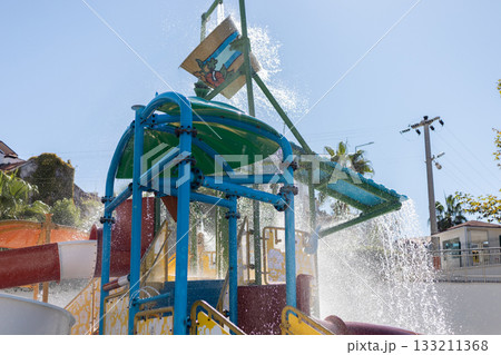 Water play structure features vibrant colors and multiple slides, with water splashing everywhere as children enjoy their time at the water park on a sunny day Water play structure features vibrant colors and multiple slides, with water splashing everywhere as children enjoy their time at the water park on a sunny day 133211368