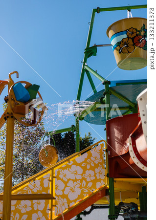 A vibrant water play area showcases colorful slides and water features. The bright blue sky adds to the fun atmosphere, inviting children to enjoy the splashes on a warm day A vibrant water play area showcases colorful slides and water features. The bright blue sky adds to the fun atmosphere, inviting children to enjoy the splashes on a warm day 133211378