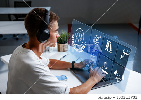 Young man using laptop with headphones while exploring legal icons on a screen 133211782