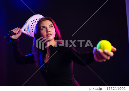 Young woman prepares to serve in a sports match with a paddle and ball in a studio Young woman prepares to serve in a sports match with a paddle and ball in a studio 133211902