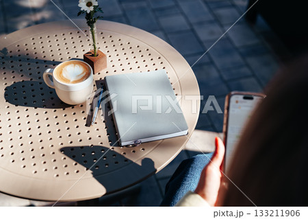 Enjoying a warm drink and writing notes at an outdoor cafe in the sunshine 133211906