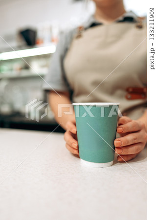Barista serving coffee in a cafe with green cup on a countertop near afternoon light Barista serving coffee in a cafe with green cup on a countertop near afternoon light 133211909