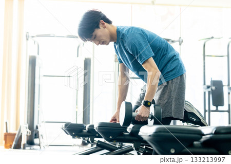 トレーニングジムでダンベルを使って筋トレする若い男性 トレーニングジムでダンベルを使って筋トレする若い男性 133213997