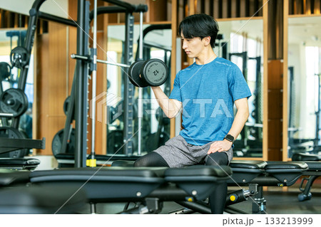 トレーニングジムでダンベルを使って筋トレする若い男性 トレーニングジムでダンベルを使って筋トレする若い男性 133213999