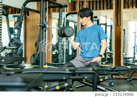 トレーニングジムでダンベルを使って筋トレする若い男性 133214000