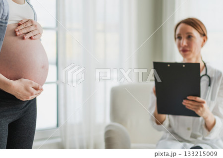 Pregnant woman hands touching big belly in doctor office. Female doctor examining pregnant woman. Gynecologist doctor consulting patient about pregnancy in hospital. Visit to doctor medical checkup 133215009