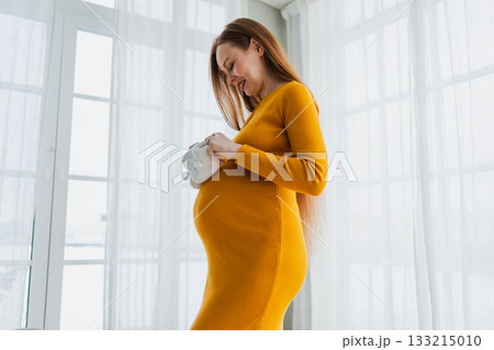 Pregnancy motherhood people expectation future. Pregnant woman with big belly holding newborn baby booties smiling at home. Young mom enjoying pregnancy. Maternity tenderness parenthood new life 133215010