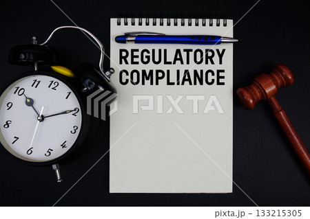 Regulatory Compliance text written on notepad with gavel and alarm clock on black background 133215305