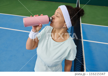 Athletic Woman Drinking Pink Smoothie On Tennis Court After Practice Athletic Woman Drinking Pink Smoothie On Tennis Court After Practice 133215347