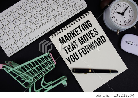 Marketing That Moves You Forward text written on notepad with keyboard and trolley shopping cart on black background 133215374