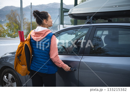 Woman With Backpack Opens Car Door For Road Trip With Roof Box On SUV Woman With Backpack Opens Car Door For Road Trip With Roof Box On SUV 133215382