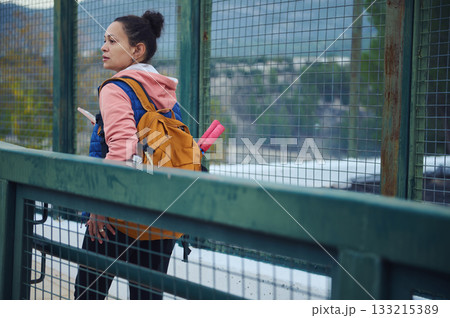 Woman With Orange Backpack On Bridge Carrying Pink Yoga Mat Looking Over City 133215389