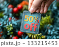 Hand holding label with 50 percent off tag over Christmas tree background. Retail promotion, holiday sale discount, festive shopping. Black Friday, Cyber Monday, New Year marketing advertisement. Hand holding label with 50 percent off tag over Christmas tree background. Retail promotion, holiday sale discount, festive shopping. Black Friday, Cyber Monday, New Year marketing advertisement. 133215453