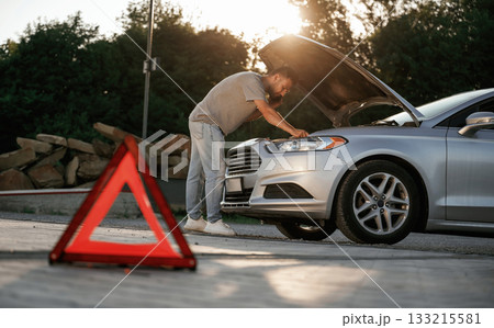 Under the sunlight, red sign, accident, broken automobile, repair. Man is with his car outdoors Under the sunlight, red sign, accident, broken automobile, repair. Man is with his car outdoors 133215581