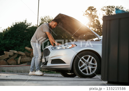 Beautiful sunlight. Hood is opened, guy is repairing the automobile. Man is with his car outdoors Beautiful sunlight. Hood is opened, guy is repairing the automobile. Man is with his car outdoors 133215586