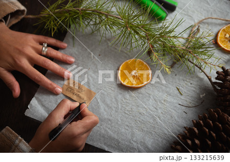 Handwriting Christmas Gift Note On Brown Tag With Pine Branch, Orange Slice, And Pinecones Handwriting Christmas Gift Note On Brown Tag With Pine Branch, Orange Slice, And Pinecones 133215639