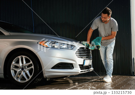 Guy is polishing the surface of automobile by using cloth. Man is with his car outdoors 133215730