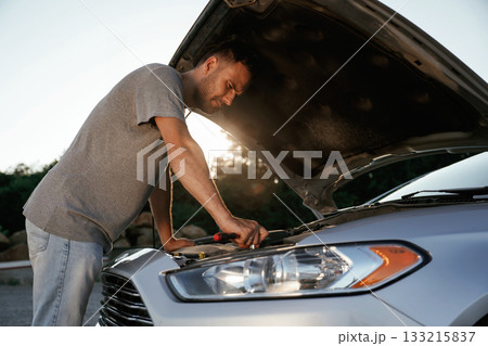 Hood is opened, repairing. Man is with his car outdoors 133215837