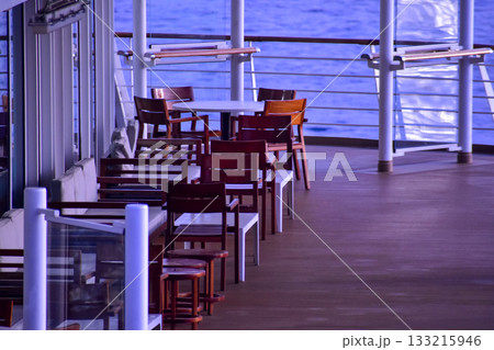 Outdoor seats on passenger ship deck with the calm seascape. Cruise ship deck. Wooden promenade deck on a luxury cruise liner. Ocean in background. 133215946