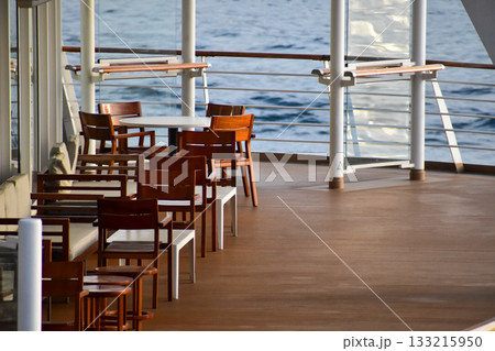 Outdoor seats on passenger ship deck with the calm seascape. Cruise ship deck. Wooden promenade deck on a luxury cruise liner. Ocean in background. Outdoor seats on passenger ship deck with the calm seascape. Cruise ship deck. Wooden promenade deck on a luxury cruise liner. Ocean in background. 133215950