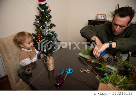 Family Christmas Craft Scene: Dad Decorating Pine Branches While Child Watches Family Christmas Craft Scene: Dad Decorating Pine Branches While Child Watches 133216118