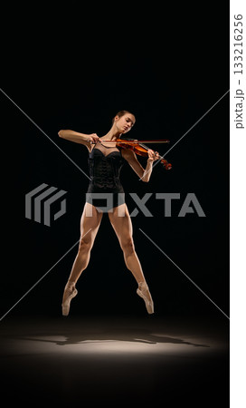 Ballerina jumping on pointe while playing violin in dramatic stage lighting. Ballerina jumping on pointe while playing violin in dramatic stage lighting. 133216256