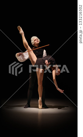 Dancer lifted in sculptural instrument-like extension by classical mentor on dark stage 133216302