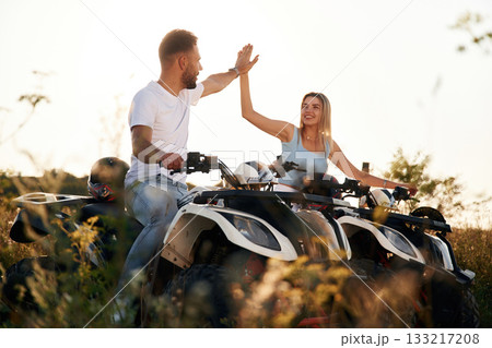 Doing high five hands gesture. Man and woman are on ATV outdoors 133217208