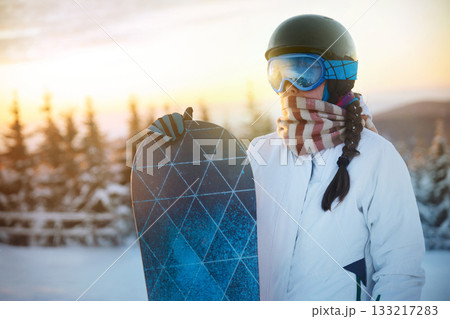 Close up of the ski goggles of a woman with the reflection of snowed mountains. Snowboarder woman on the sunset background. A mountain range reflected in the ski mask. Winter Sports 133217283
