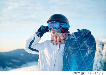Portrait Of Woman Holding a Snowboard And Wearing Ski Glasses. Ski Goggles Of Snowboarder With The Reflection Of Snowed Mountains. Winter Sports 133217317