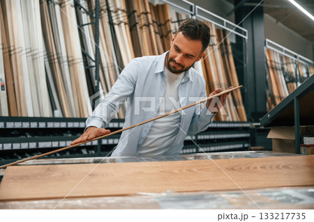 Quality of the wood in parquet, checking. Man is in the hardware shop 133217735