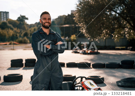 Standing against vehicle and trees. Man is outdoors, kart racing conception Standing against vehicle and trees. Man is outdoors, kart racing conception 133218481