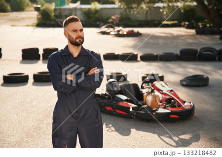 Standing with arms crossed. Man is outdoors, kart racing conception 133218482