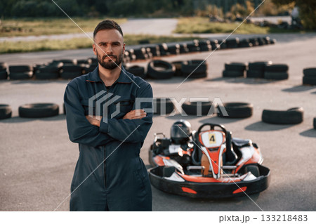 Standing with arms crossed. Man is outdoors, kart racing conception 133218483
