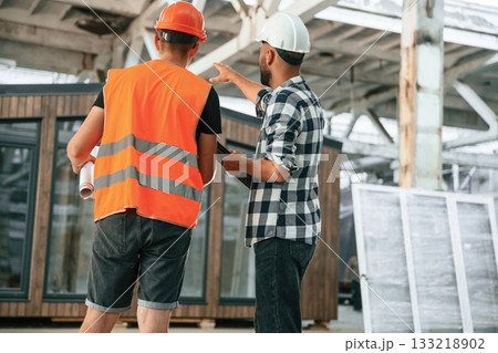 Builder is talking with manager or architect. Two workers are in the industrial wooden warehouse 133218902